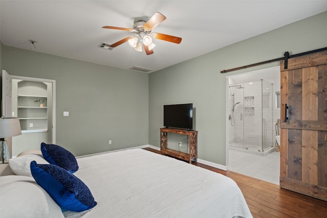 bedroom featuring visible vents, a barn door, a ceiling fan, and wood finished floors