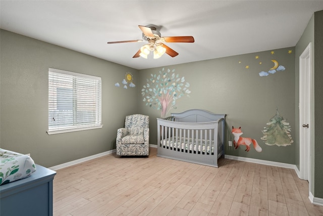 bedroom with a crib, baseboards, a ceiling fan, and wood finished floors