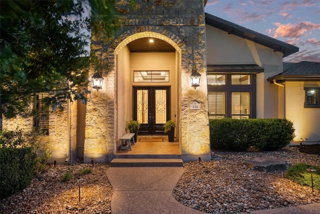exterior entry at dusk with french doors, stucco siding, and stone siding