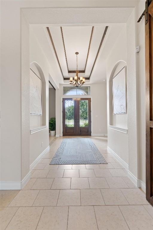 entrance foyer with light tile patterned flooring, a barn door, a chandelier, french doors, and a tray ceiling