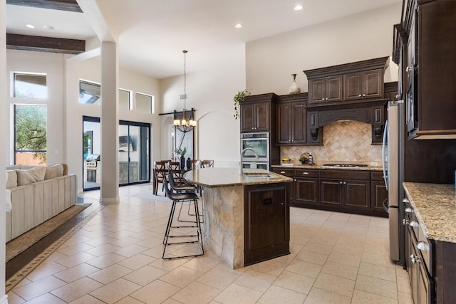 kitchen featuring appliances with stainless steel finishes, light stone counters, a kitchen breakfast bar, a chandelier, and tasteful backsplash