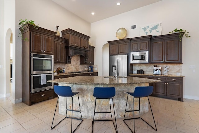 kitchen featuring a kitchen breakfast bar, backsplash, visible vents, arched walkways, and stainless steel appliances
