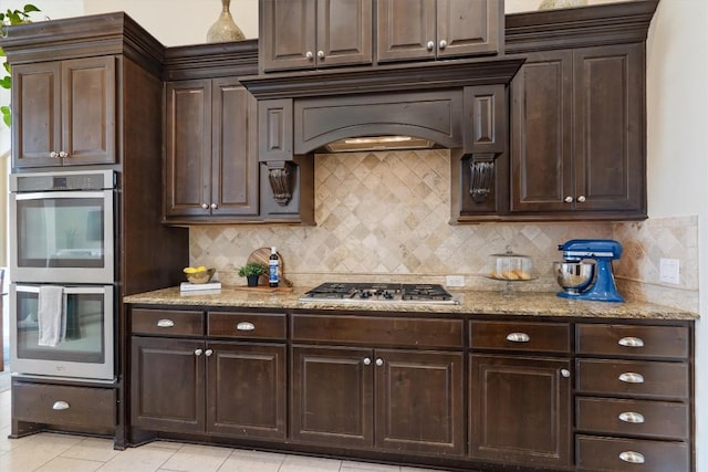 kitchen featuring light stone counters, backsplash, stainless steel appliances, and dark brown cabinets
