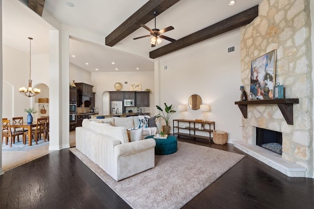 living room with a fireplace, beamed ceiling, ceiling fan with notable chandelier, and dark wood-style flooring