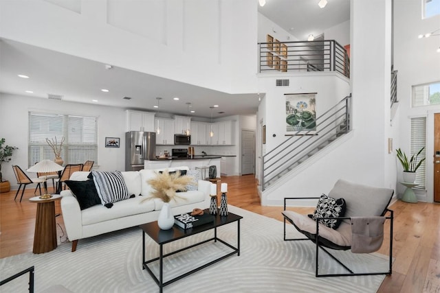 living area featuring a high ceiling, light wood finished floors, stairs, and visible vents