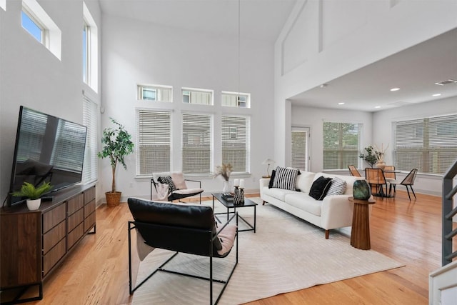 living room with a towering ceiling, recessed lighting, visible vents, and light wood-type flooring