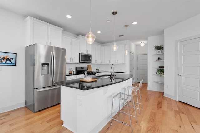 kitchen with appliances with stainless steel finishes, dark countertops, a sink, white cabinets, and light wood finished floors