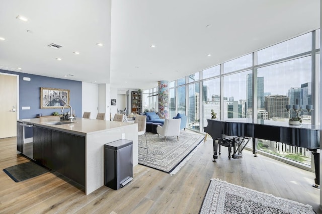 kitchen featuring a sink, light wood-style floors, an island with sink, a view of city, and visible vents