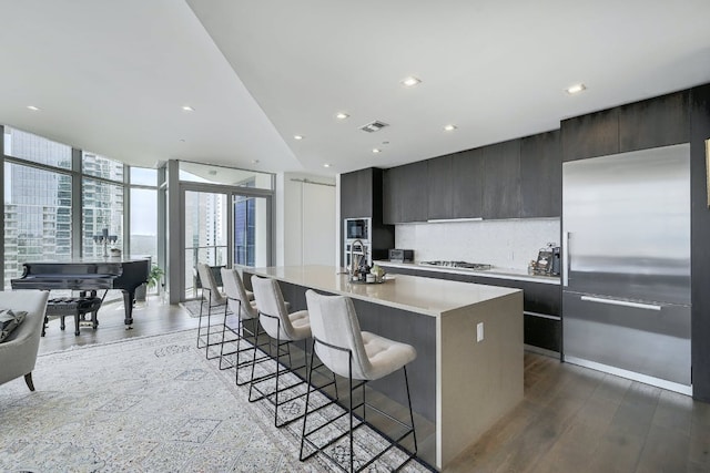 kitchen featuring built in appliances, a kitchen island with sink, modern cabinets, a kitchen bar, and light countertops