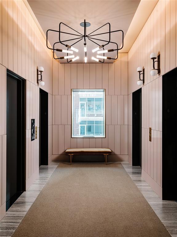 hall featuring light wood-type flooring, elevator, and a chandelier