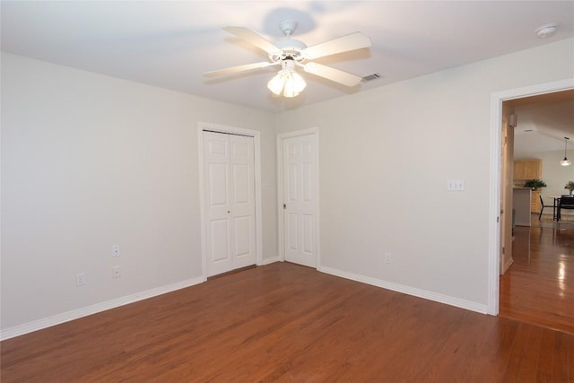 empty room with baseboards, ceiling fan, wood finished floors, and visible vents