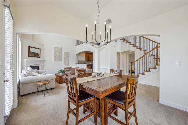 dining room with an inviting chandelier, stairs, carpet flooring, a fireplace, and arched walkways