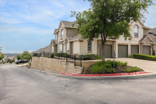view of home's exterior featuring a residential view, a garage, fence, concrete driveway, and stone siding