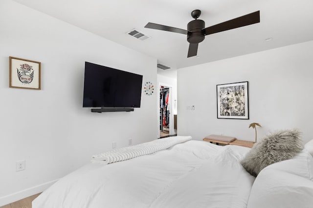 bedroom featuring a walk in closet, a ceiling fan, wood finished floors, and visible vents