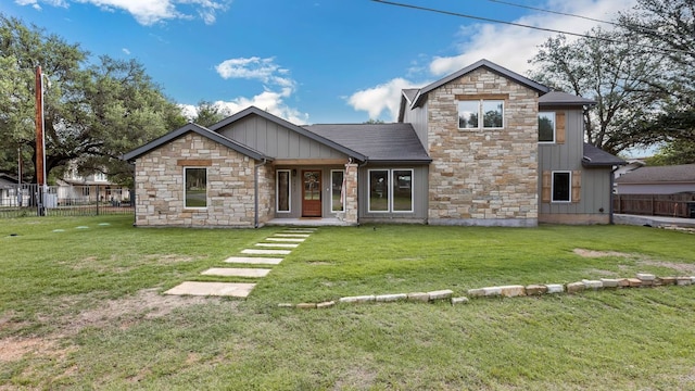 view of front of home featuring fence, board and batten siding, a front yard, and stone siding