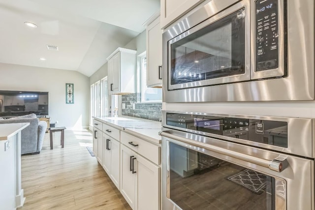 kitchen featuring backsplash, visible vents, appliances with stainless steel finishes, white cabinets, and lofted ceiling