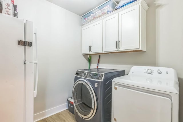 laundry room featuring light wood-style floors, separate washer and dryer, baseboards, and cabinet space