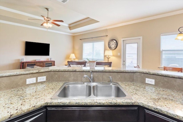 kitchen featuring crown molding, light stone countertops, ceiling fan, a sink, and a raised ceiling