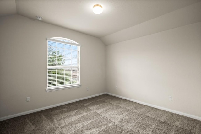 carpeted empty room featuring baseboards and vaulted ceiling