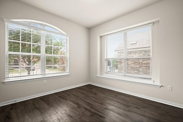 empty room with dark wood-type flooring, baseboards, and a wealth of natural light