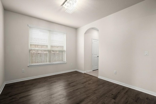 spare room featuring arched walkways, baseboards, and wood finished floors