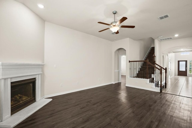 unfurnished living room featuring arched walkways, a fireplace with raised hearth, wood finished floors, and stairway