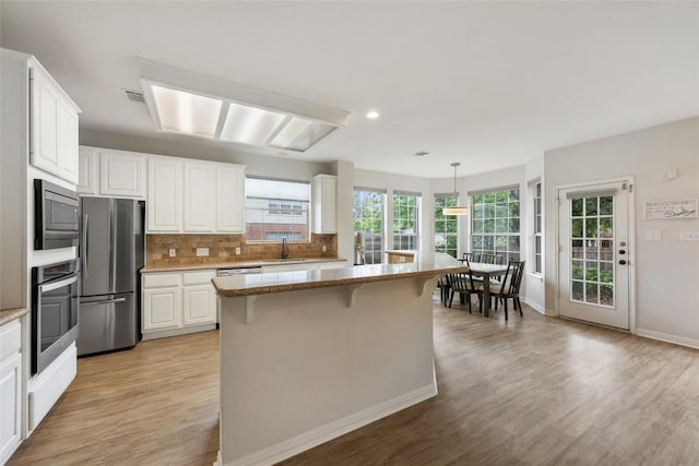2045 Saint Andrews Dr, Round Rock, TX 78664 - kitchen with light wood-style flooring, appliances with stainless steel finishes, backsplash, white cabinetry, and a breakfast bar