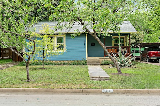 view of front facade with roof with shingles, a detached carport, a porch, and a front lawn