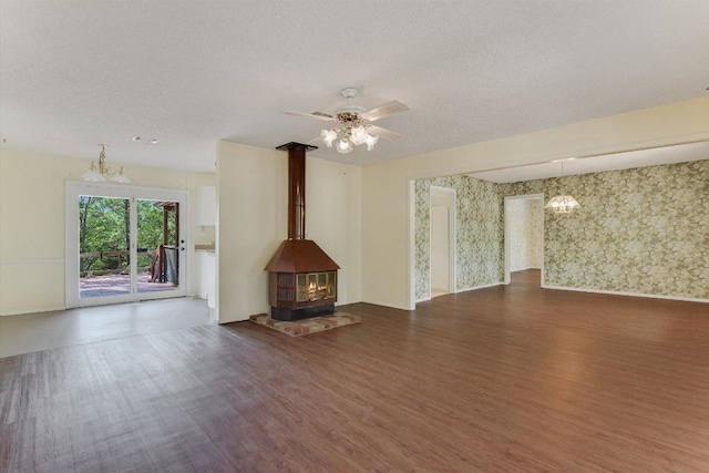 unfurnished living room with a textured ceiling, ceiling fan, wood finished floors, and a wood stove