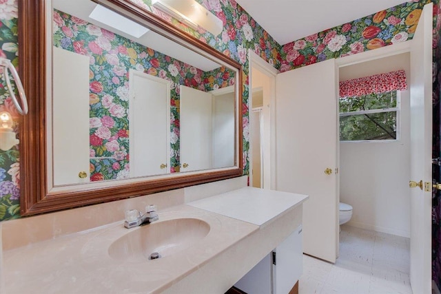 bathroom with vanity, baseboards, toilet, and wallpapered walls