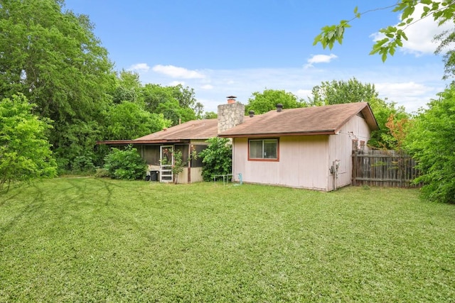 rear view of property with a lawn, fence, a chimney, and a sunroom