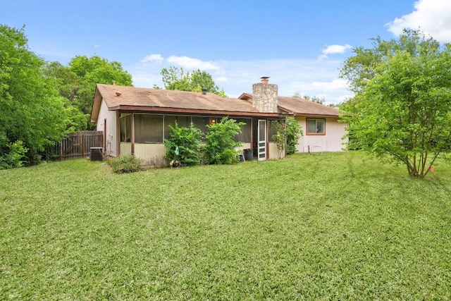rear view of house featuring a sunroom, a lawn, and a chimney