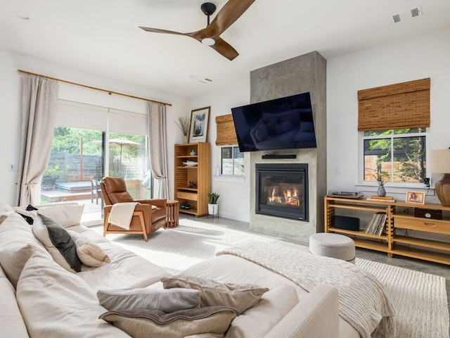 living area with visible vents, a ceiling fan, plenty of natural light, and a large fireplace