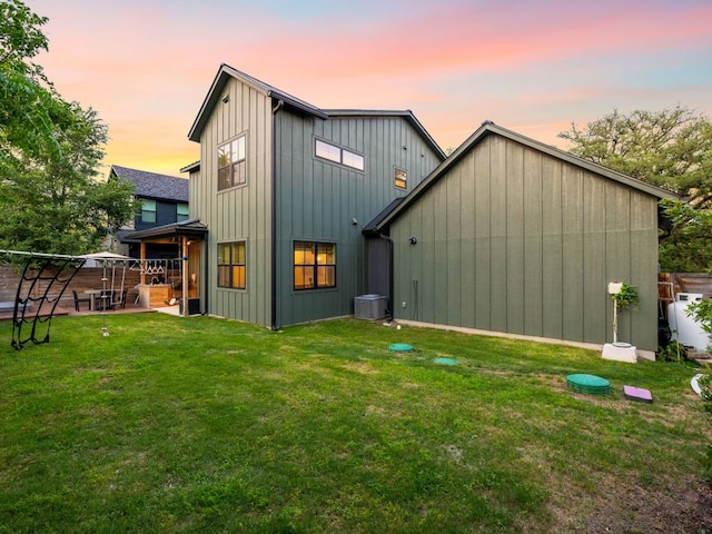 back of house at dusk with a lawn, board and batten siding, a patio, and cooling unit