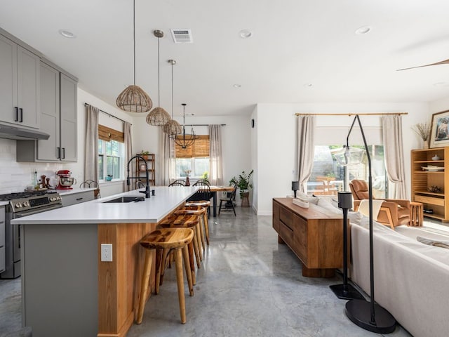 kitchen with concrete flooring, a sink, gray cabinetry, stainless steel gas range, and under cabinet range hood