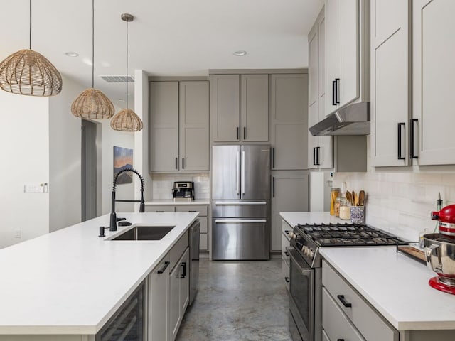 kitchen with concrete flooring, gray cabinets, under cabinet range hood, a sink, and stainless steel appliances
