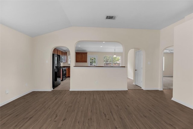 unfurnished living room featuring visible vents, arched walkways, vaulted ceiling, wood finished floors, and baseboards