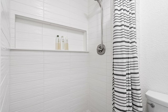 full bath featuring a textured wall, toilet, and tiled shower
