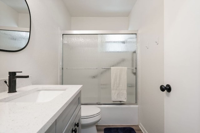 full bathroom with vanity, bath / shower combo with glass door, wood finished floors, and toilet