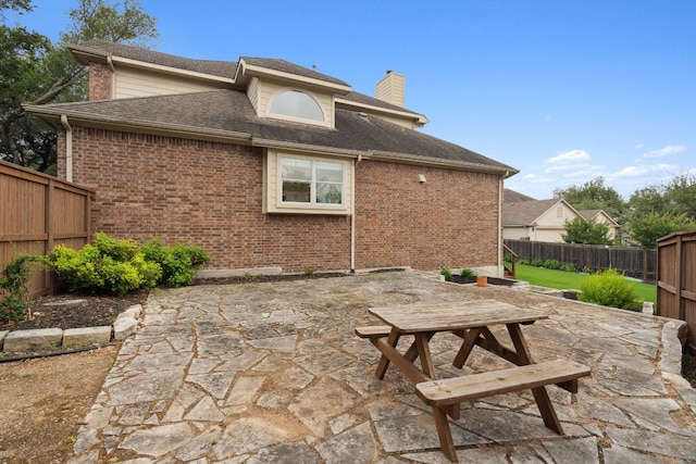 rear view of house with a fenced backyard, outdoor dining space, a chimney, and a patio area
