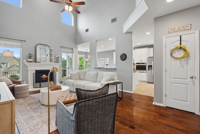 living area with a ceiling fan, visible vents, wood finished floors, and a towering ceiling