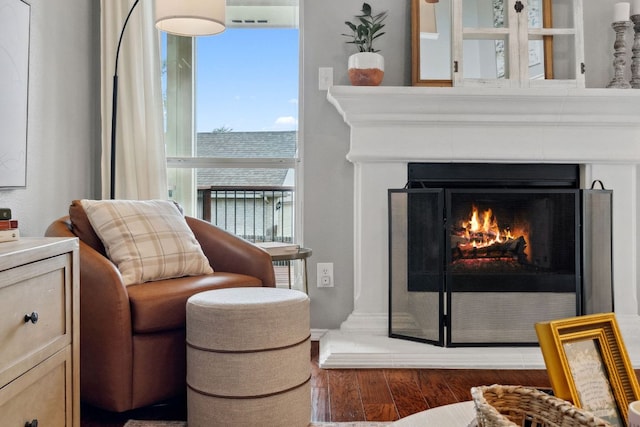 sitting room with wood finished floors, a healthy amount of sunlight, and a lit fireplace