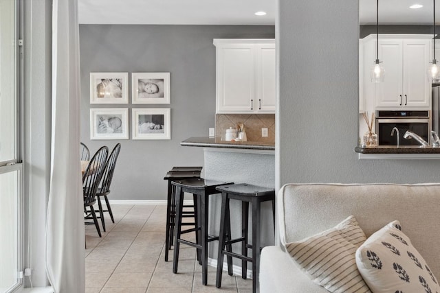 kitchen featuring dark countertops, tasteful backsplash, light tile patterned floors, stainless steel oven, and white cabinetry