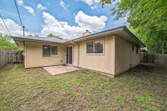 back of property with a lawn, a patio, a chimney, and a fenced backyard