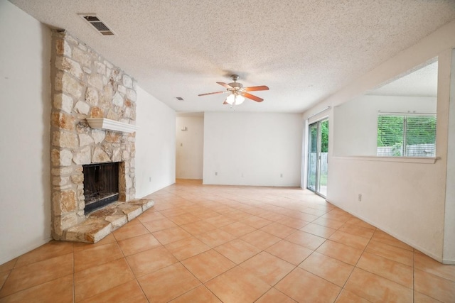 unfurnished living room featuring visible vents, light tile patterned flooring, a stone fireplace, a textured ceiling, and a ceiling fan