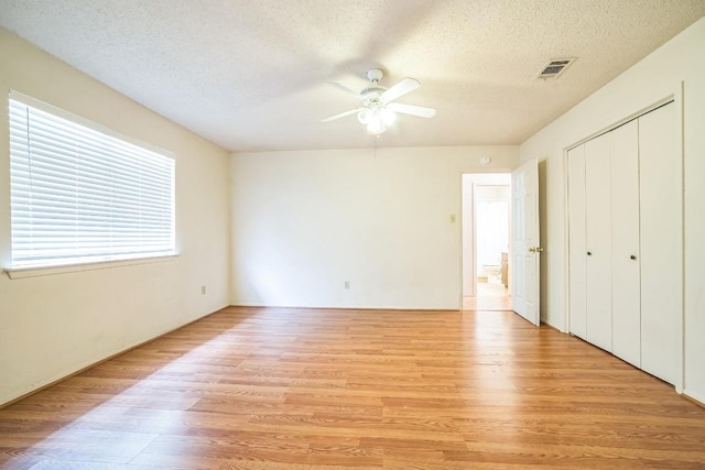 unfurnished bedroom with light wood finished floors, a textured ceiling, a ceiling fan, visible vents, and a closet