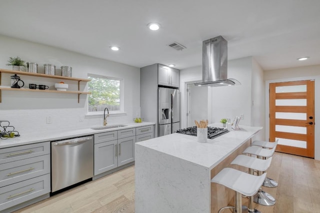 5307 Downs Dr, Austin, TX 78721 - kitchen with appliances with stainless steel finishes, a sink, island exhaust hood, gray cabinets, and a breakfast bar