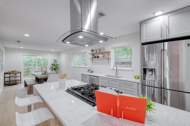 kitchen with island exhaust hood, visible vents, appliances with stainless steel finishes, light wood-type flooring, and a sink