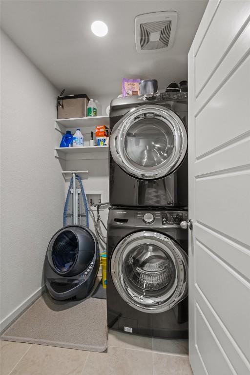 laundry room featuring laundry area, stacked washer and clothes dryer, tile patterned floors, and visible vents