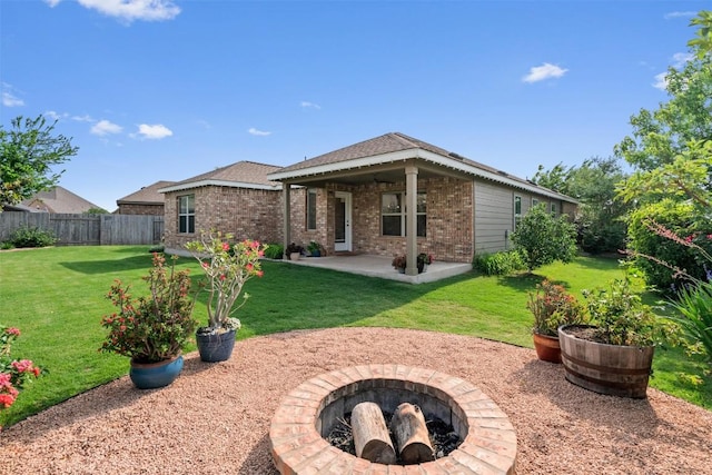 back of property with a fire pit, fence, brick siding, a patio area, and a yard
